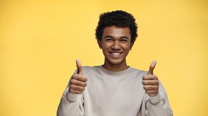 happy african american teenager in sweatshirt showing thumbs up isolated on yellow