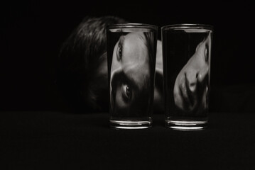 black and white strange portrait of a man looking through two glasses of water