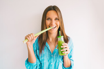 Healthy detox vegan diet. Young beautiful woman eating a stick of green organic celery and drinking fresh homemade celery juice from a glass bottle. Healthy dieting eating and drinking lifestyle