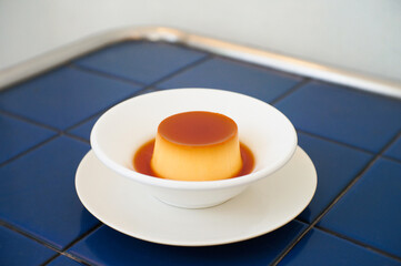 Caramel custard pudding in a dish placed on a blue table.