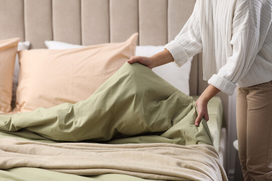 Woman making bed with new pistachio linen in room, closeup