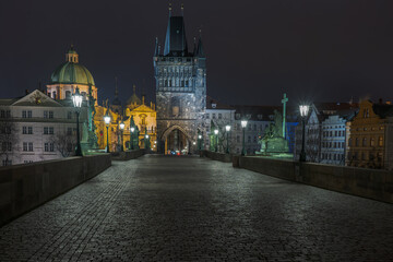 Fototapeta na wymiar sidewalk with cobblestones and a tower on Charles Bridge and lanterns lit on it at night in the center of Prague