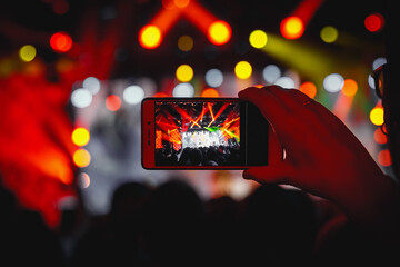 Hand with the smartphone turned on to record or take pictures during the live concert.