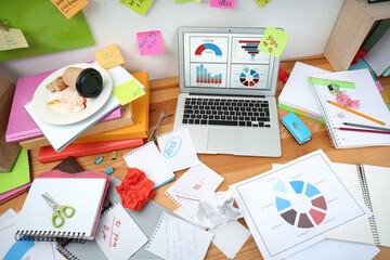 Messy table with laptop and stationery. Concept of being overwhelmed by work