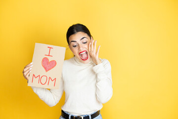 Beautiful woman celebrating mothers day holding poster love mom message shouting and screaming loud down with hands on mouth