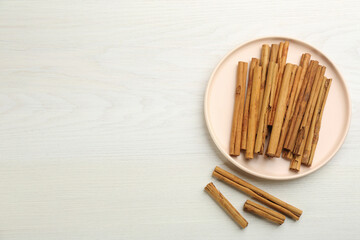 Aromatic cinnamon sticks on white wooden table, flat lay. Space for text
