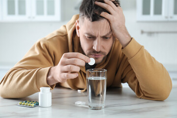 Man taking medicine for hangover at table in kitchen