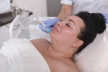 Obraz na płótnie Canvas Charming plus size woman getting facial microdermabrasion treatment on her chin at beauty salon