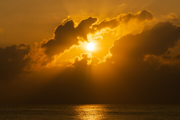 The Sun rising through clouds over the sea background