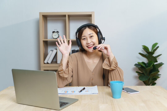 Smiling Asian young female student using headset listen on laptop screen while talking and learning online courses. Chinese business woman wear headphones working with video call for customer service
