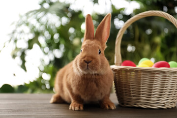 Cute bunny and basket with Easter eggs on table against blurred background