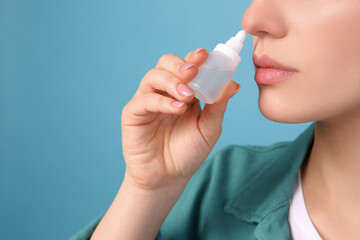 Woman using nasal spray on light blue background, closeup - obrazy, fototapety, plakaty