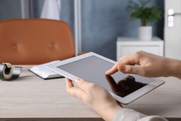 Woman using modern tablet at workplace indoors, closeup