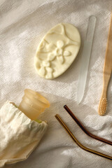 Sustainable toiletries and utensils on linen cloth: metal straws, wooden toothbrush, glass nail file, bar of soap and menstrual cup. Top view.