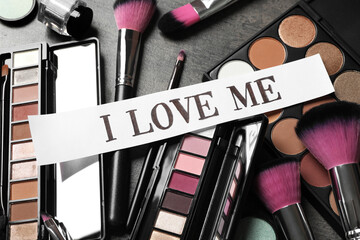 Paper with phrase I Love Me and different makeup products on table, above view