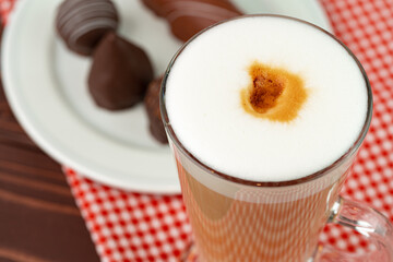 Cup of coffee and saucer with chocolate sweets on wooden table