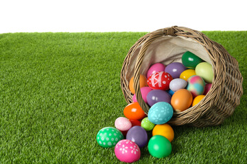 Wicker basket with Easter eggs on green grass against white background. Space for text