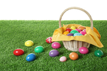 Wicker basket with Easter eggs on green grass against white background. Space for text