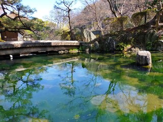 Fototapeta na wymiar 史跡和歌山城の日本庭園（紅葉谷庭園）の池の水に映り込んだ空と橋の冬の風景（コピースペースあり）