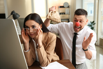 Man popping paper bag behind his colleague in office. Funny joke - obrazy, fototapety, plakaty