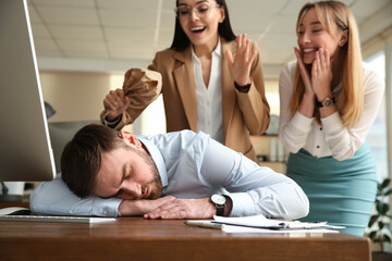 Young women popping paper bag their behind sleeping colleague in office. Funny joke