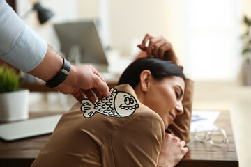 Man sticking paper fish to colleague's back while she sleeping in office, closeup. Funny joke