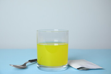 Glass of dissolved medicine, sachet and spoon on turquoise table