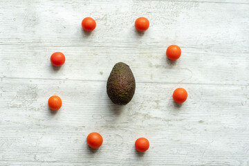 avocado and fresh cherry tomatoes on white wooden background with conceptual shapes