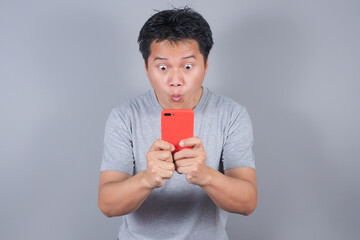Asian man looks surprised at the good news he received from his smartphone. Men show shocked movements with bulging eyes while  on smartphone on gray background