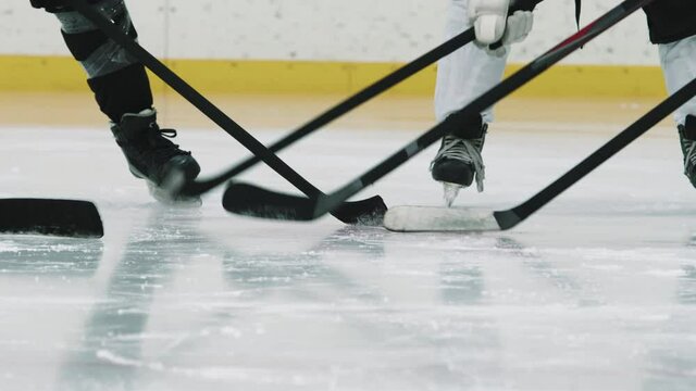 Panning low-section shot with slowmo of unrecognizable male hockey players standing in circle tapping their sticks on ice