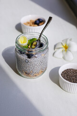 Jar with chia pudding, granola, blueberries, plumeria flower.