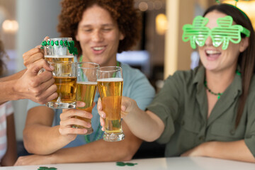 Diverse group of happy friends celebrating st patrick's day making toast with glasses of beer at bar