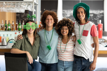 Portrait of diverse group of happy friends celebrating st patrick's day embracing at a bar