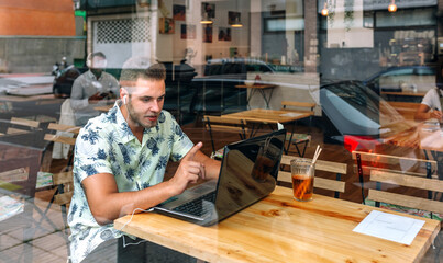 Young man with earphones working with laptop from coffee shop