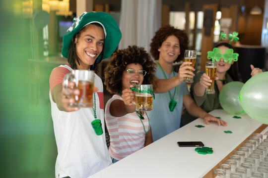 Diverse group of happy friends celebrating st patrick's day raising glasses of beer at a bar - Powered by Adobe