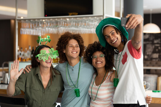 Diverse group of happy friends celebrating st patrick's day taking selfie at bar