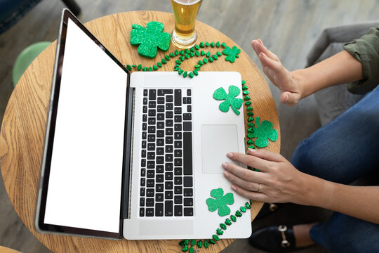 Caucasian woman waving making st patrick's day video call with laptop at a bar - Powered by Adobe