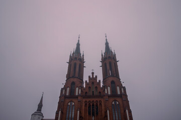 Part of the church building with two towers on a cloudy and foggy morning.