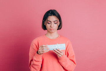 Portrait of upset frustrated girl opening gift box isolated on pink background