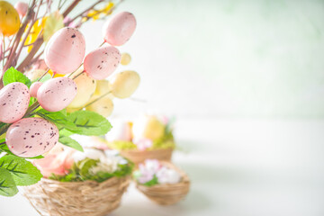 Obraz na płótnie Canvas Easter greeting card background. Spring tree decor branches with colorful eggs, flowers and leaves on white background copy space for your text