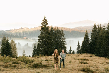 Beautiful young couple in dark green clothes walk by the hands in the mountains in nature