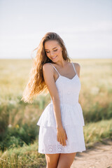 Fototapeta na wymiar Young woman with long hair in a white dress walks in sunny weather