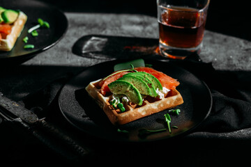 Belgian waffles with salmon, avocado and cream cheese on a black plate. Healthy breakfast