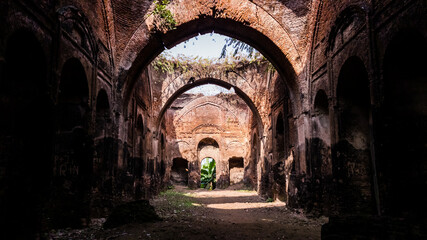 Obraz premium The arches in the overgrown ruins of an ancient dilapidated mosque in the town of Murshidabad in West Bengal, India.