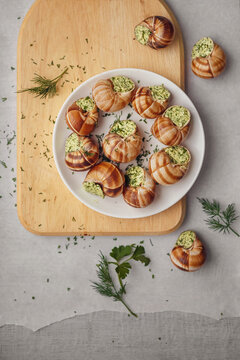 Burgundy escargots with green oil and parsley on a light board