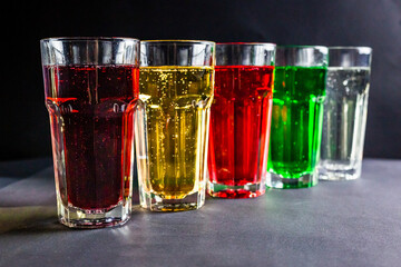 Assorted colored soda in the glasses on the black background.