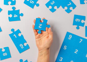 Woman hand holding  puzzle piece,  autism symbol.  Blue puzzle jigsaw with numbers on a white background. April 2, Autism World Awareness day. Top view.