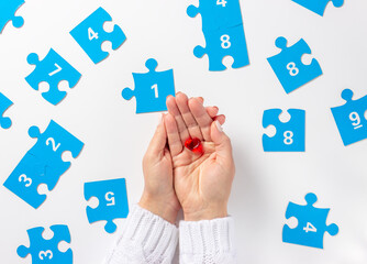 Woman hand holding heart. Blue puzzle jigsaw with numbers on a white background. April 2, Autism World Awareness day. Top view.