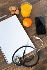 Top view of a doctor's work desk. Notebook, stethoscope and mobile phone on dark wood background. 