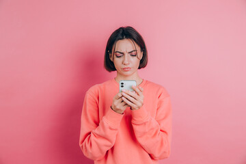Young woman is feeling sad unhappy angry while reading sms using her mobile phone, over pink...